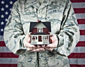 Person in military fatigues holding a model of a house