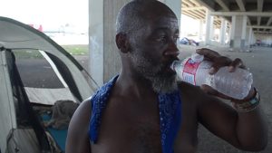 Photo of a person drinking from a plastic water bottle with a tent in the background