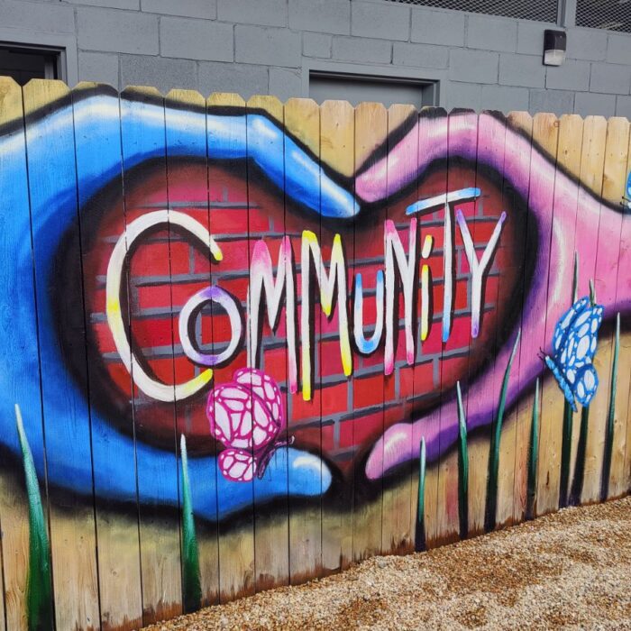 mural on wooden fence of hands in heart shape and text that says community