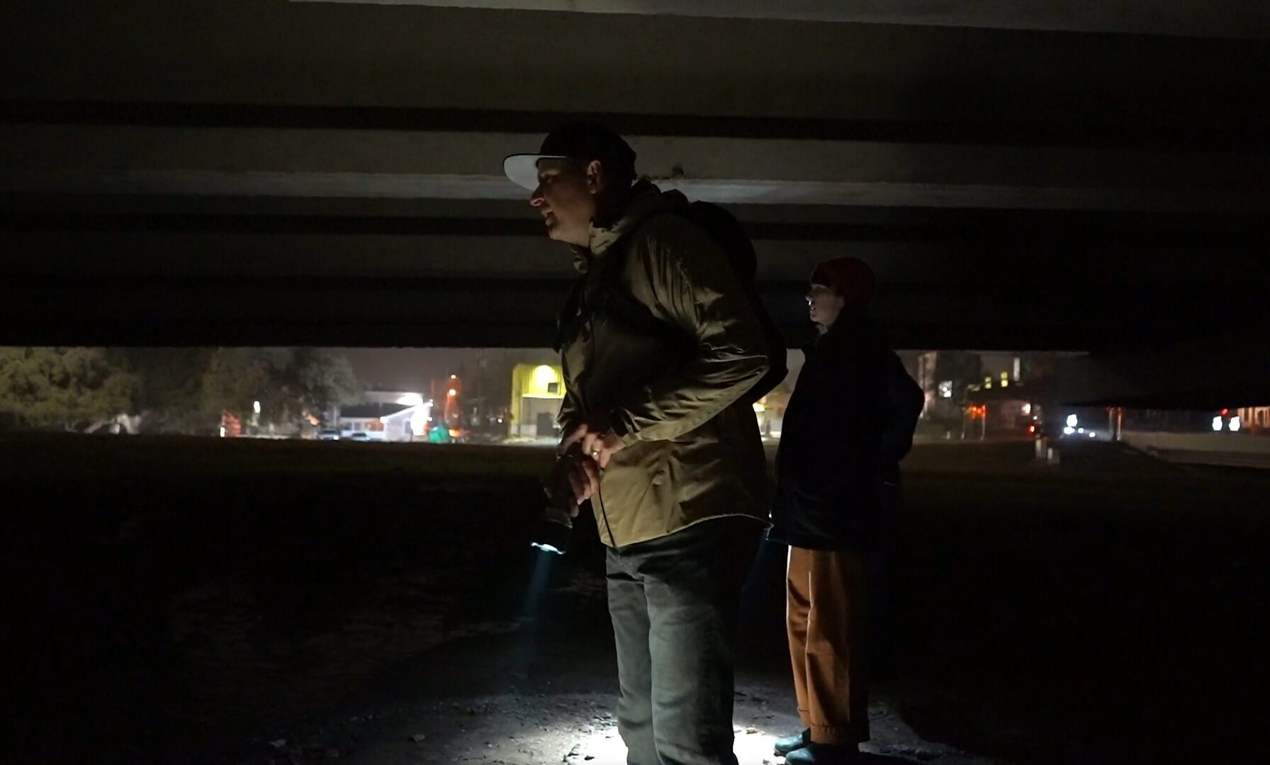 People stand under a bridge at night with flashlights